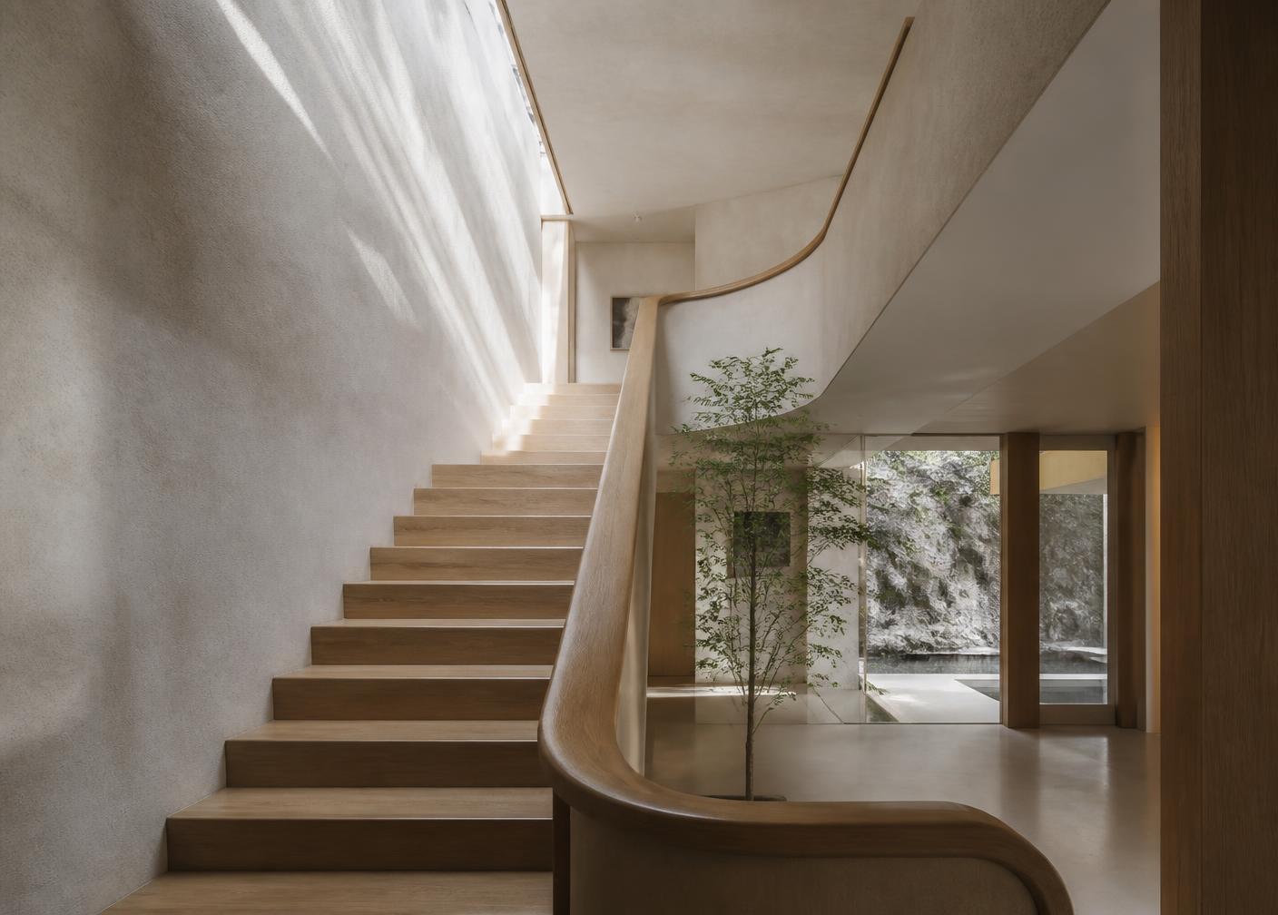 Sunlit modern stairwell with pale plaster walls and a sculptural oak handrail